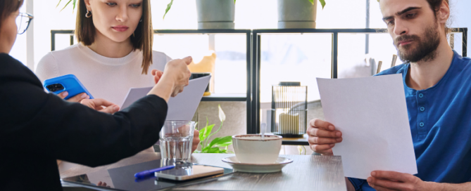 Two young adults reviewing documents with a financial adviser at a table, discussing factors that affect credit scores and how to improve them.